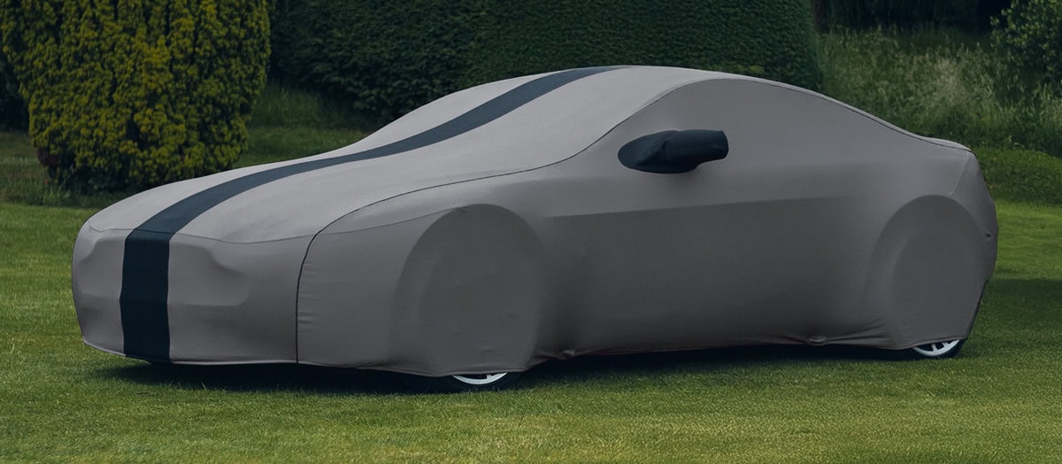 An Aston Martin with a custom indoor cover on it in grey with a black stripe and piping.