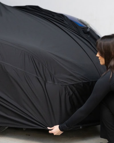 A person stretching a car cover onto a car.